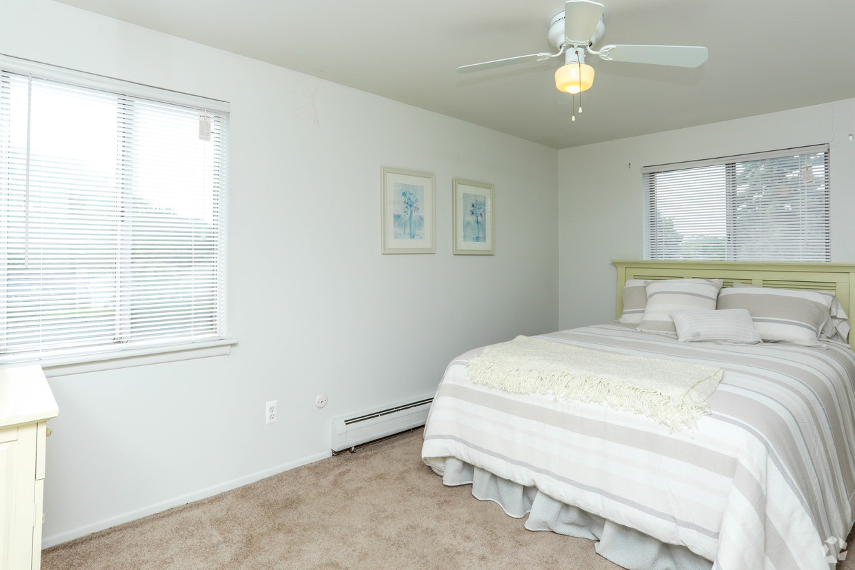 A bedroom with white walls and beige carpet.